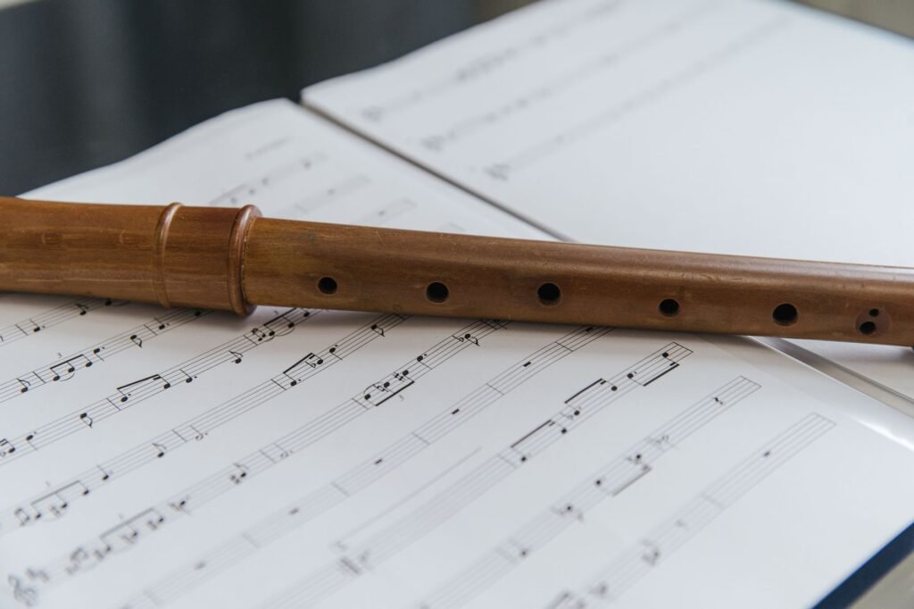 Simple wooden flute with finger holes resting across pages of open sheet music