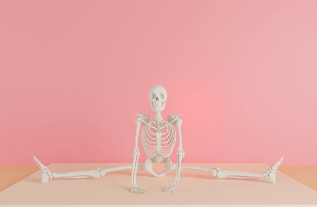 White anatomical skeleton model posed doing the splits against a pink wall