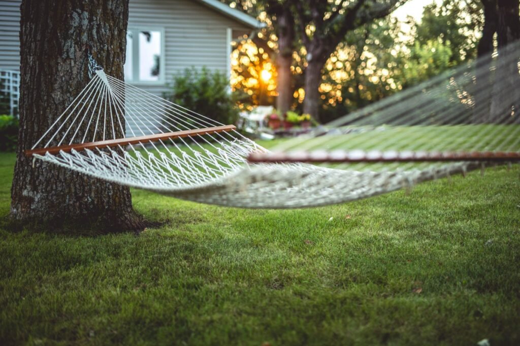 Empty white rope hammock strung beneath a tree over a green lawn at sunset