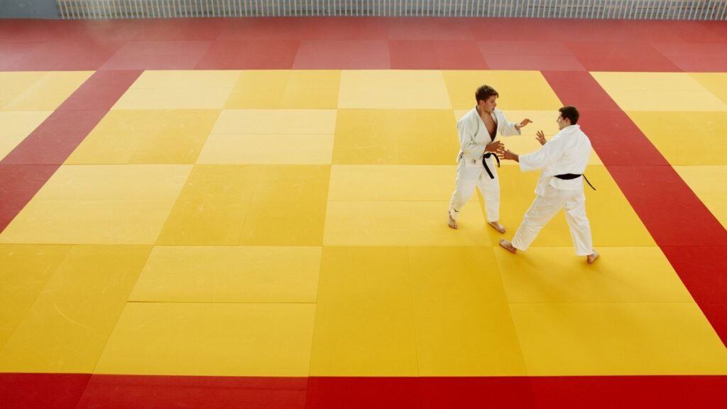 Two people in white uniforms gripping each other on a yellow and red practice mat