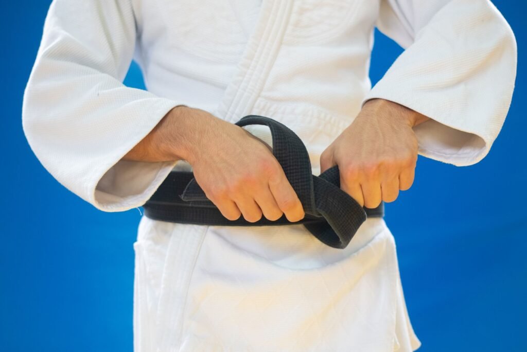 Person in a white martial arts uniform tightening a black belt at the waist