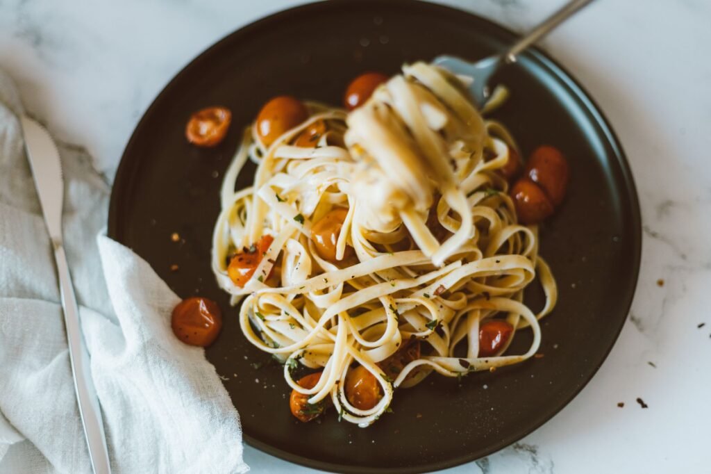 Close-up of a delicious Italian pasta dish with cherry tomatoes on a dark plate, garnished with herbs.