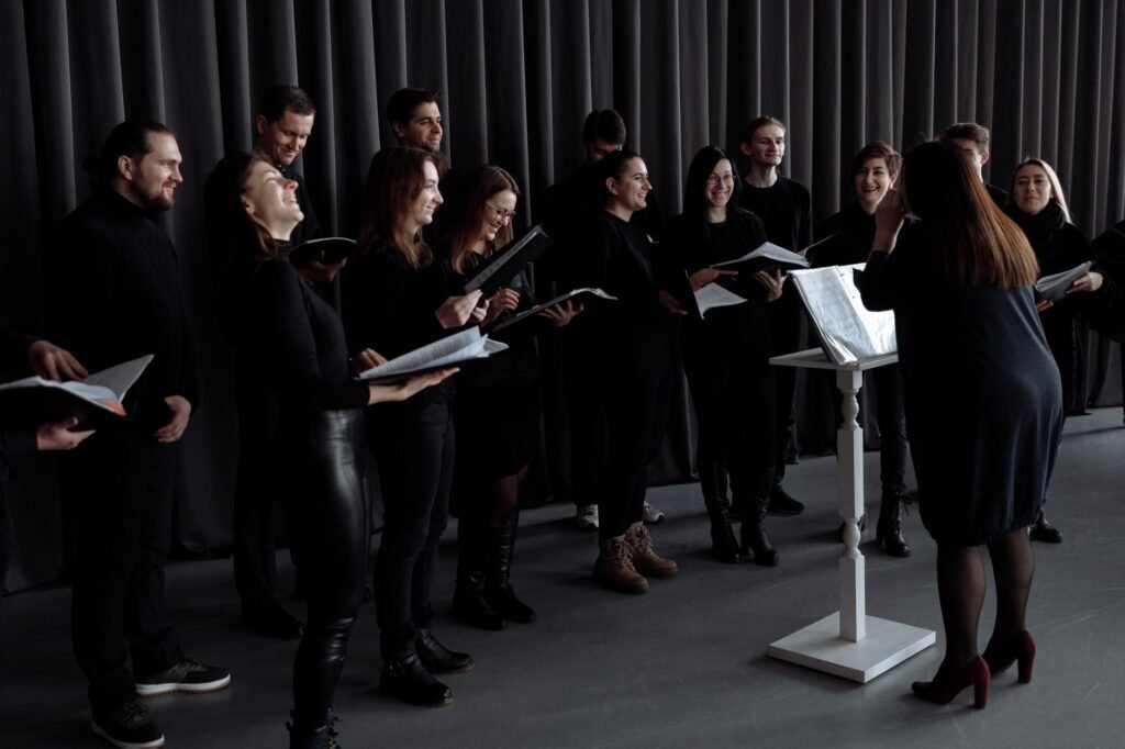 Choir dressed in black holding music folders on stage while a conductor leads from a music stand