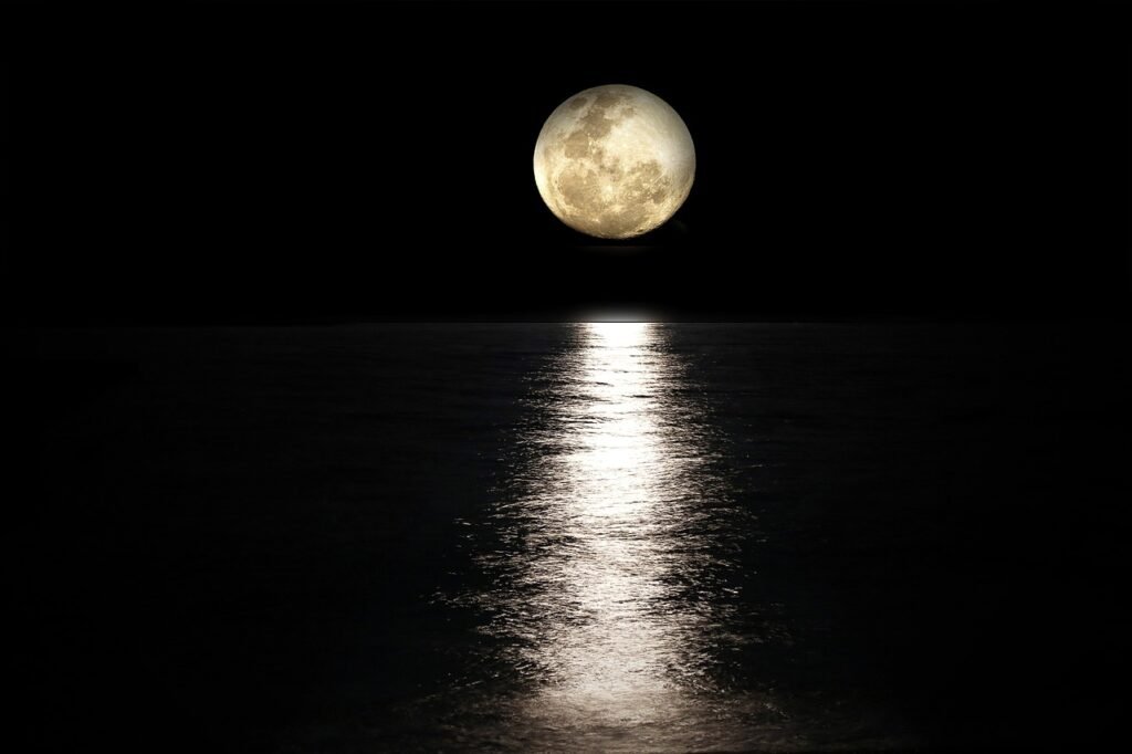 Bright full moon above a dark sea casting a long shimmering reflection on the water