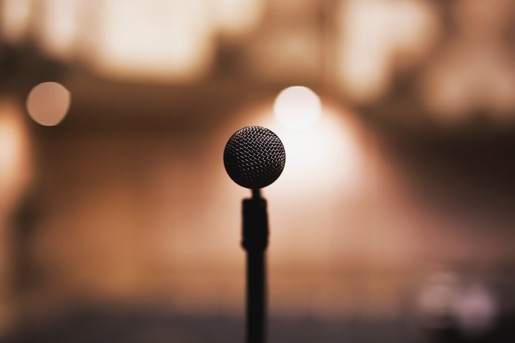 Microphone on a stand silhouetted against warm blurred stage lights in a dark room