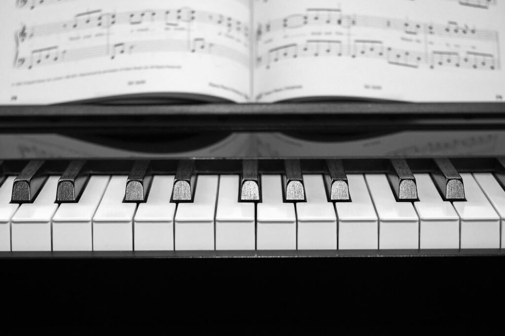 Open book of sheet music resting above a row of black and white piano keys