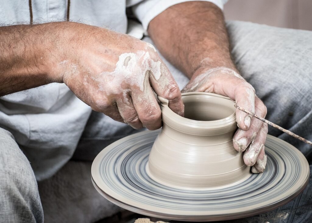 Clay covered hands shaping a small pot on a spinning pottery wheel