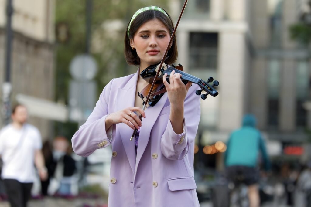 Young woman in a lavender blazer playing violin on a busy city sidewalk