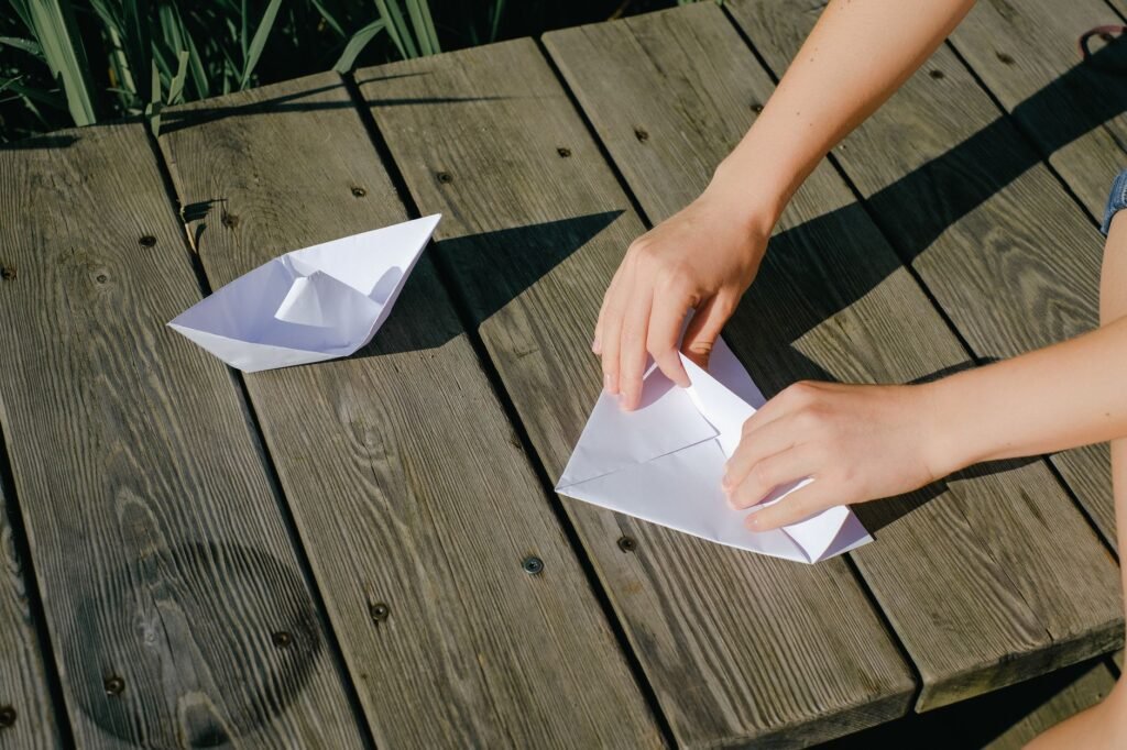 Close-up of hands folding paper boats on a wooden deck, perfect for creative and leisure-themed concepts