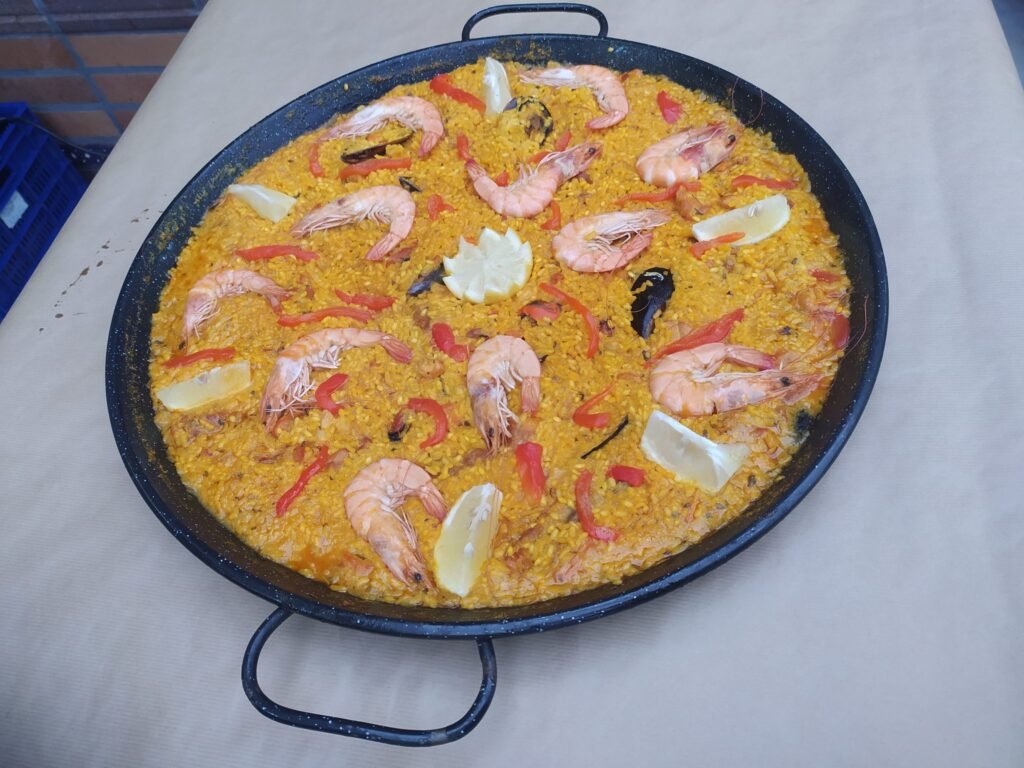 A large black paella pan containing a traditional Spanish seafood paella. The dish features yellow rice wit...