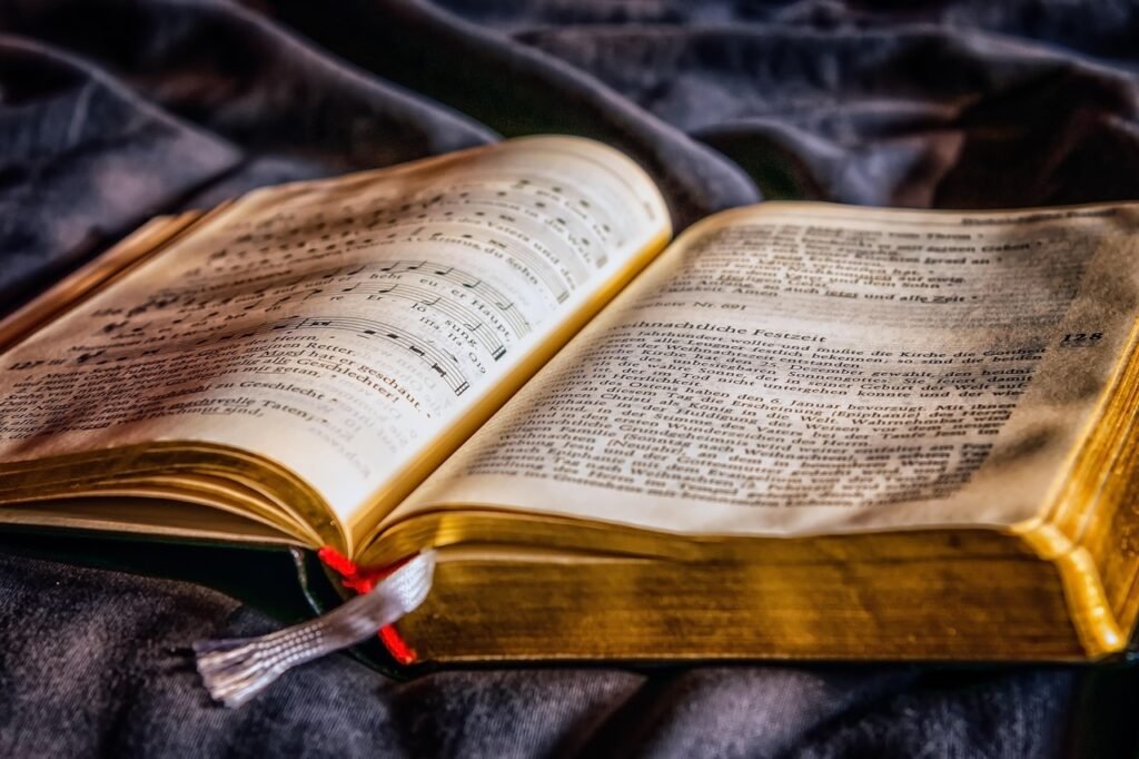 Worn open book with gilded page edges and a ribbon bookmark resting on dark fabric