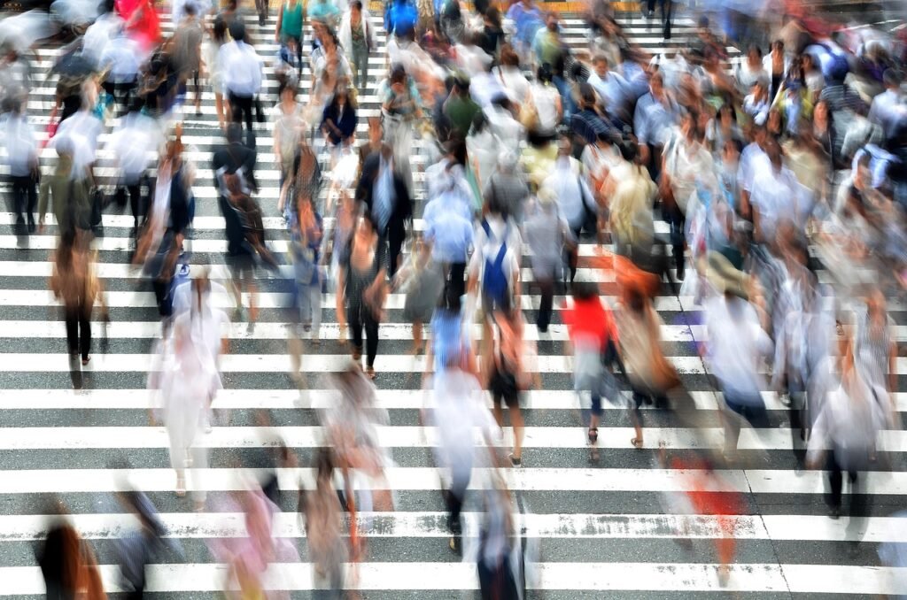 Motion blurred crowd of pedestrians rushing across a wide striped crosswalk in the city
