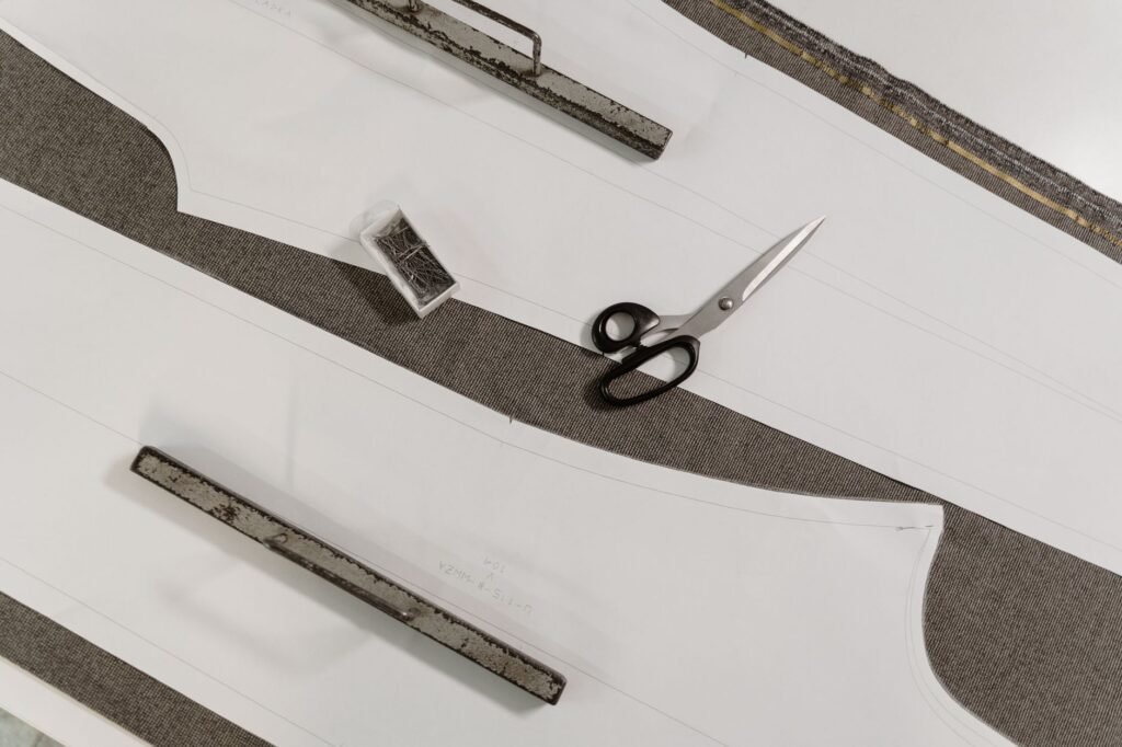 Paper sewing pattern pieces laid on gray fabric with scissors and two metal bars