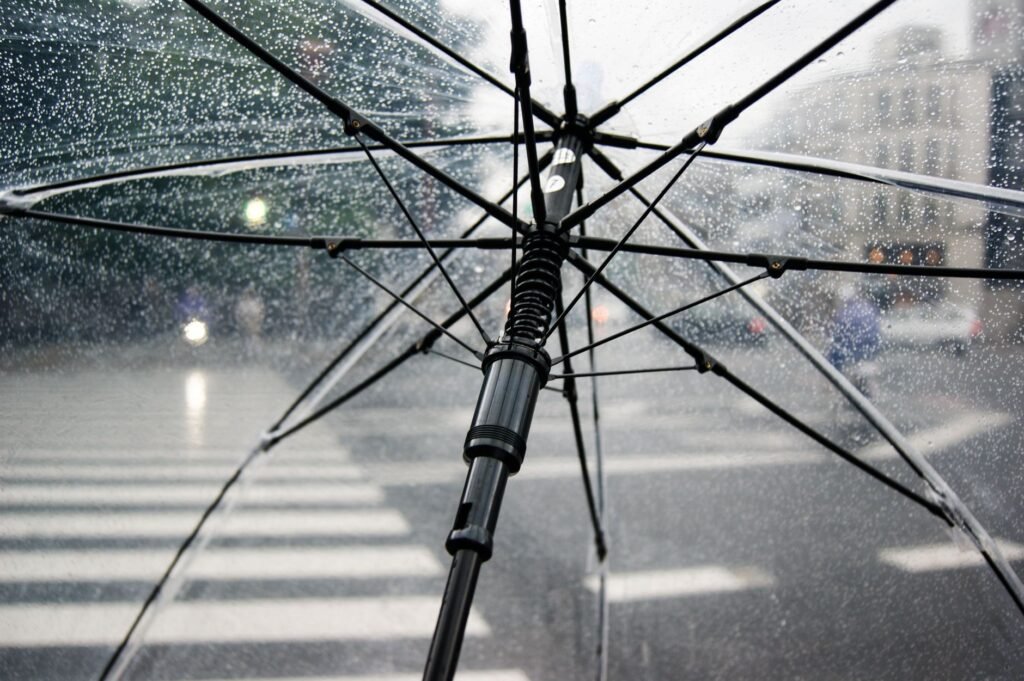 Looking up through a clear umbrella dotted with raindrops above a wet street crosswalk