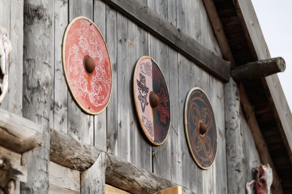 Three round painted shields hanging on the weathered plank wall of a wooden building