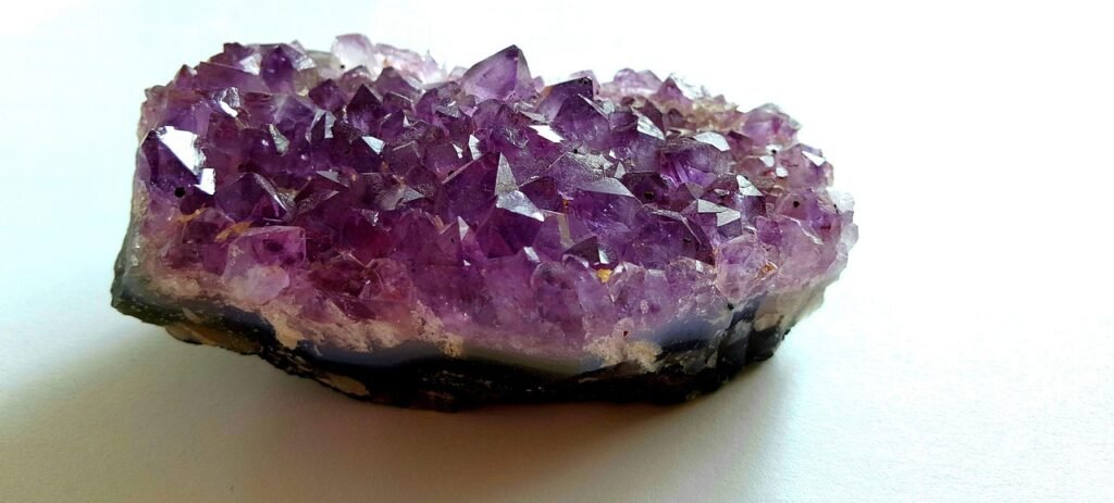 Purple amethyst crystal cluster with pointed tips resting on a white surface