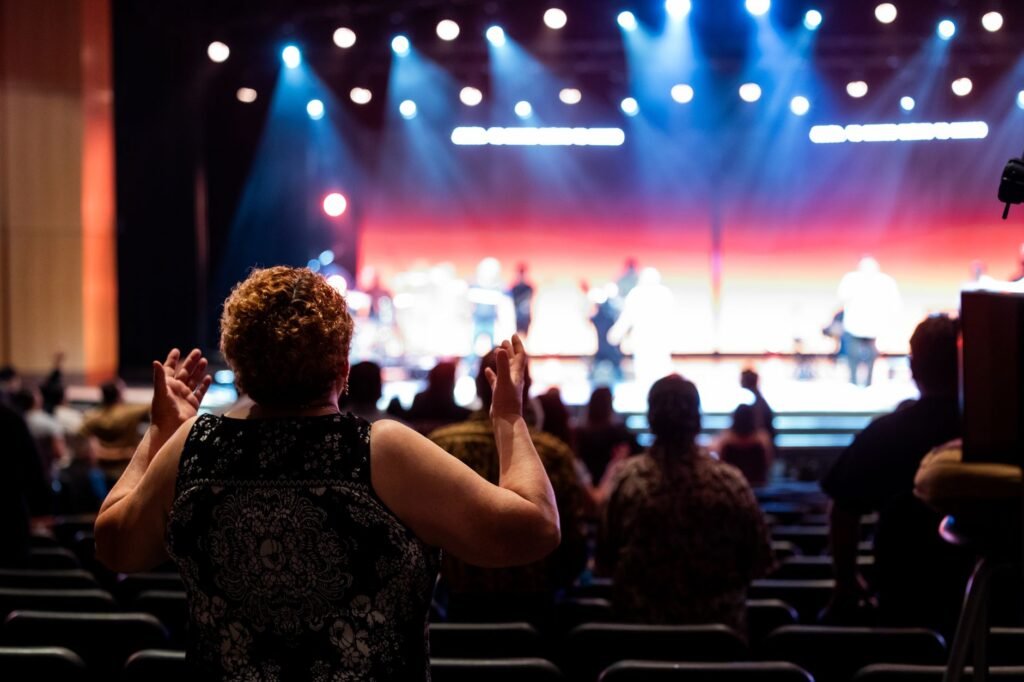 Audience member applauding with raised hands toward a brightly lit stage with performers