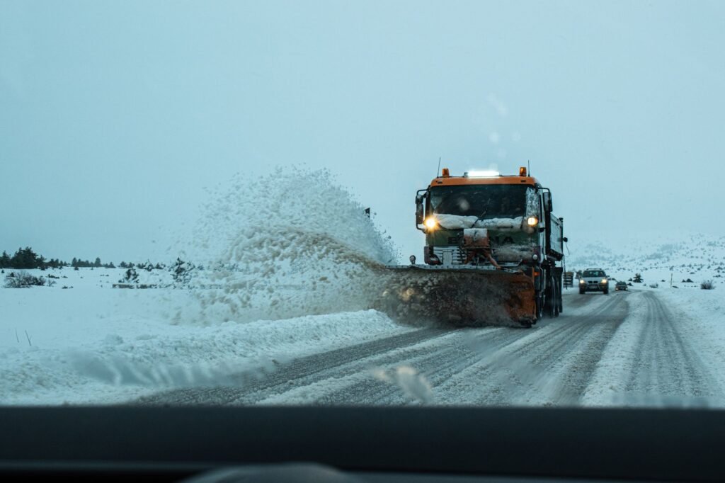 Orange snowplow truck throwing snow aside on a winter road seen through a windshield
