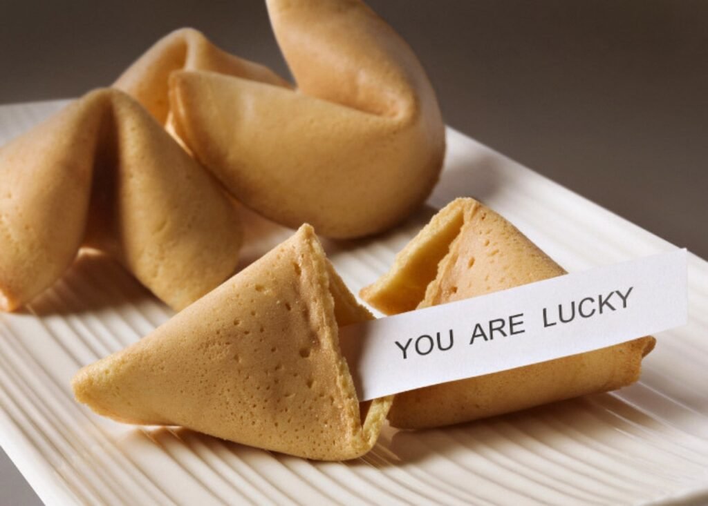 Golden fortune cookies on a white ridged plate, one holding a paper fortune slip