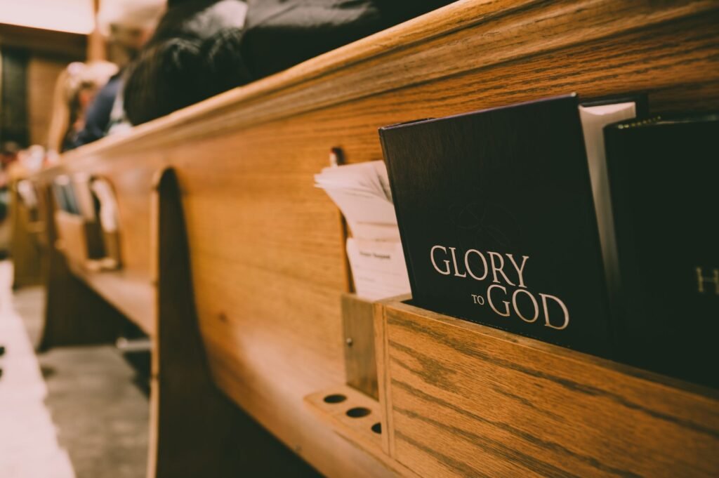 A close-up of a wooden church pew holding hymnals and a Bible, symbolizing worship