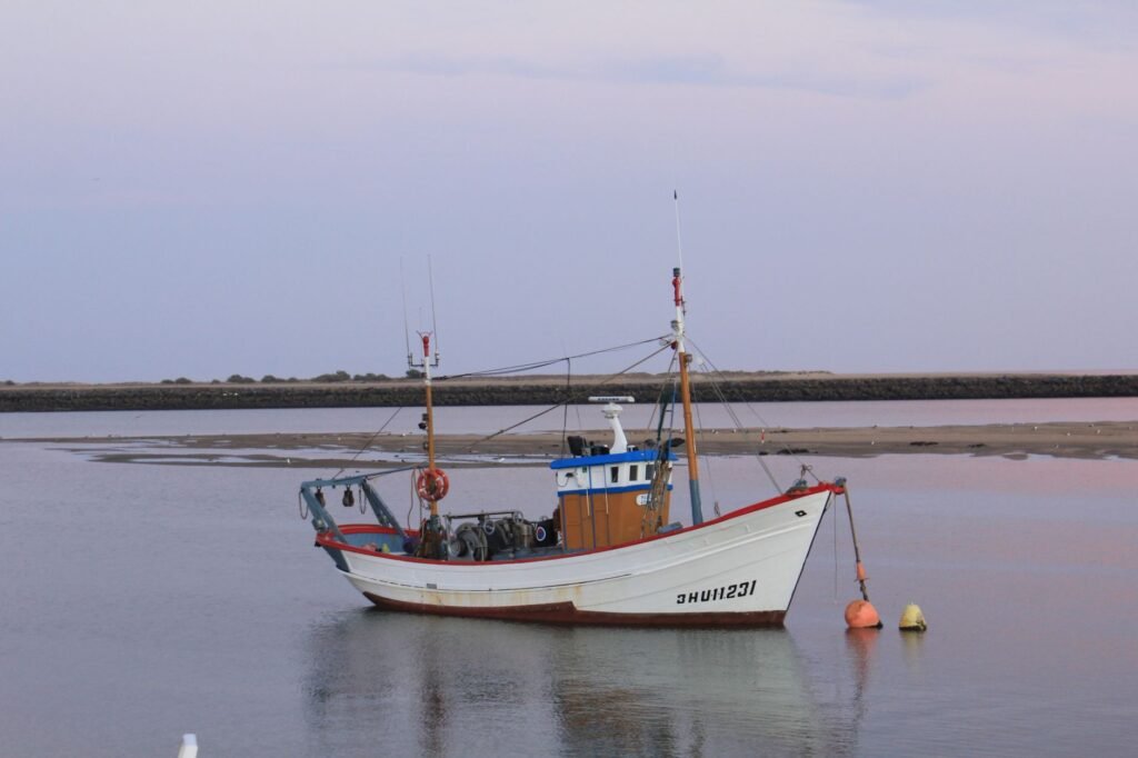 Small fishing boat with a white hull moored on calm still water under a pale pink sky