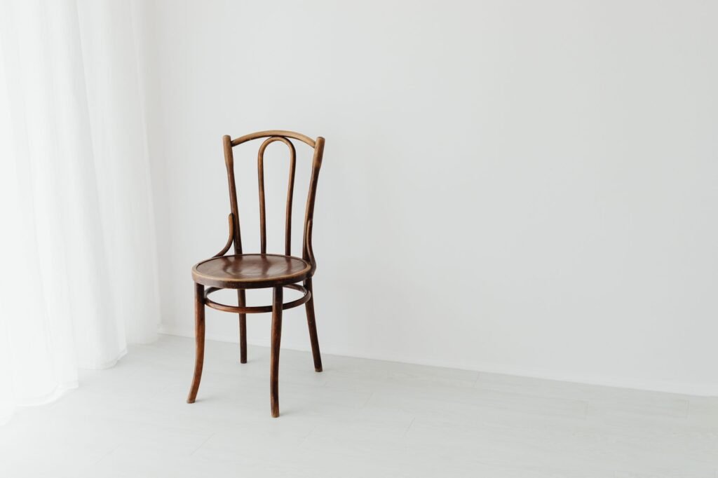 A simple wooden chair sits in a bright, minimalist interior with a white background