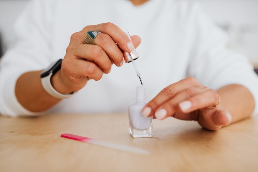 Close-up of hands applying lilac nail polish with a visible file on a wooden surface.