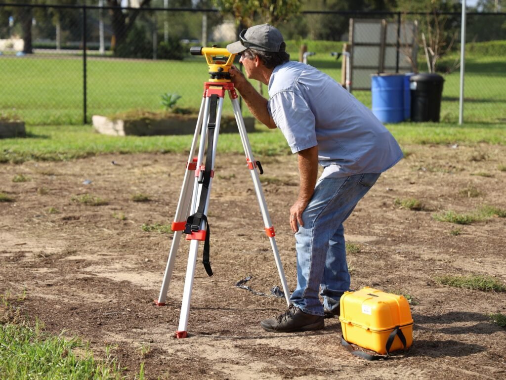 Surveyor bending to look through a leveling instrument on a tripod at a dirt site