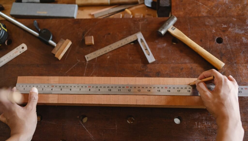 Hands measuring a wooden board with a steel ruler beside metal squares on a workbench