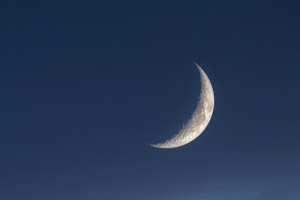 Thin crescent moon glowing against a deep blue evening sky