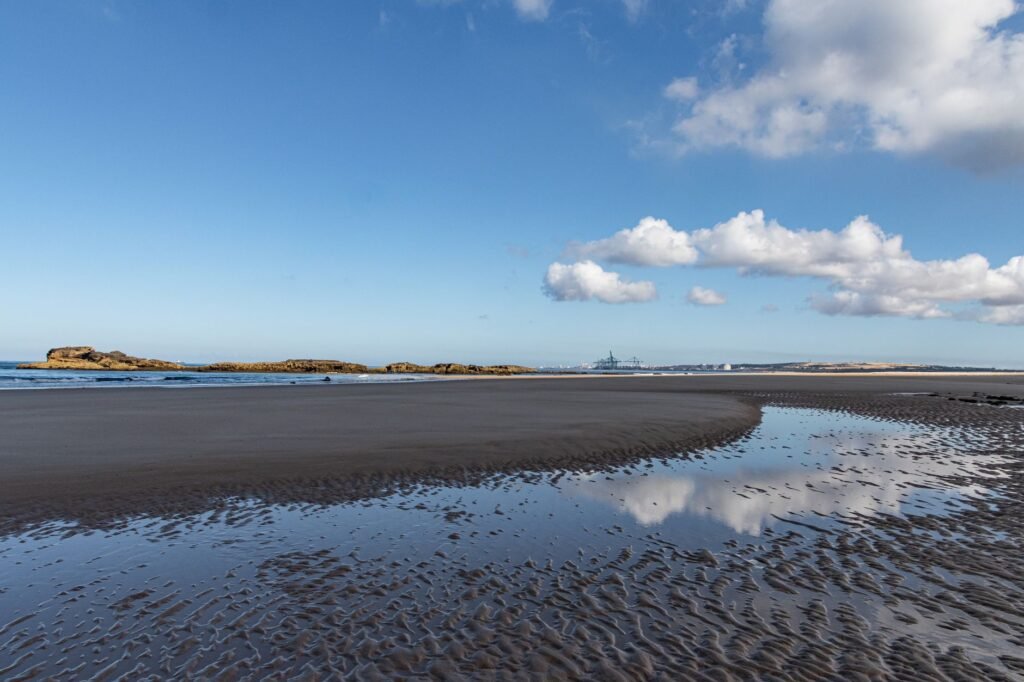 Wet rippled sand and shallow tidal pools reflecting clouds on a wide beach at low water