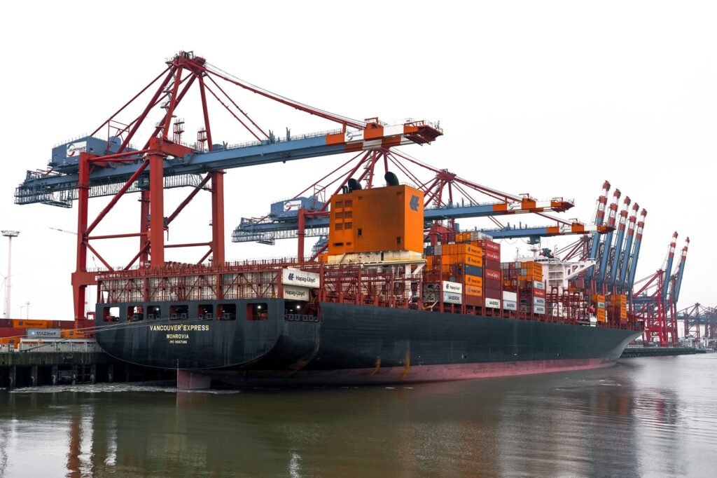 Loaded container ship moored under tall red cranes at a busy cargo terminal