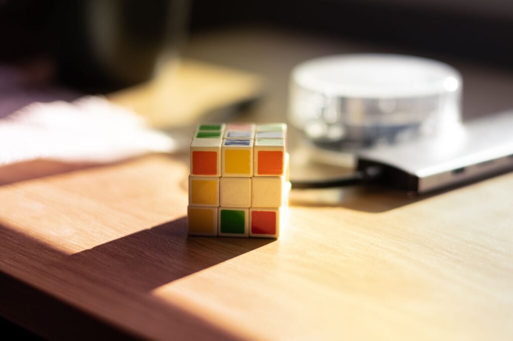 Scrambled colorful puzzle cube sitting on a sunlit wooden desk