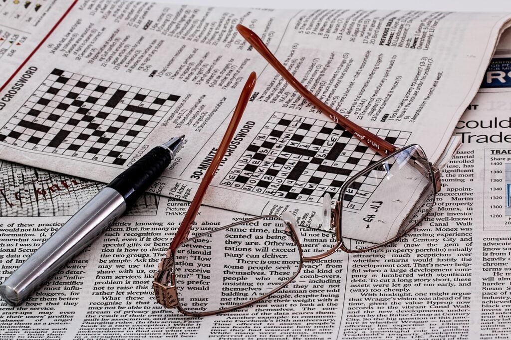 Newspaper crossword grids with reading glasses and an uncapped pen lying across the page