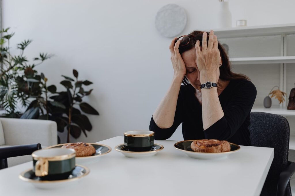 A woman in emotional distress sits at a table with coffee and pastries, illustrating loneliness and sadness