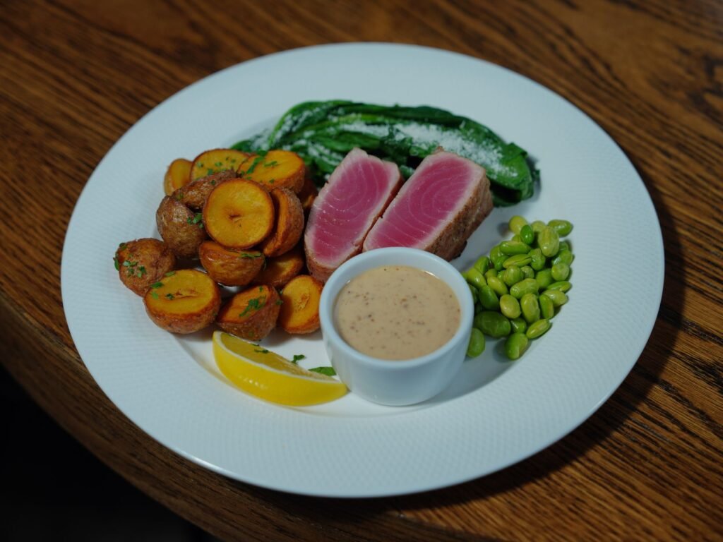 Seared fish slices with rosy centers on a white plate with roasted potatoes and greens