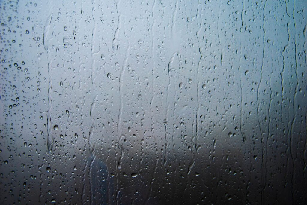Raindrops and streaks running down a window pane against a dim gray sky