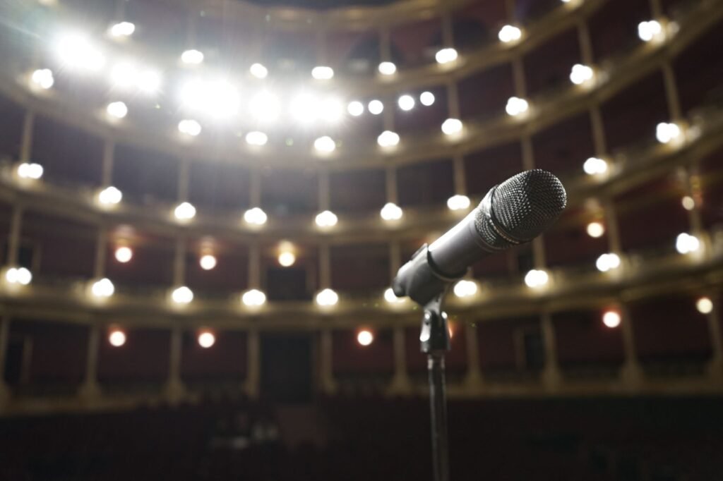 Microphone on a stand facing rows of lit balconies in an empty theater