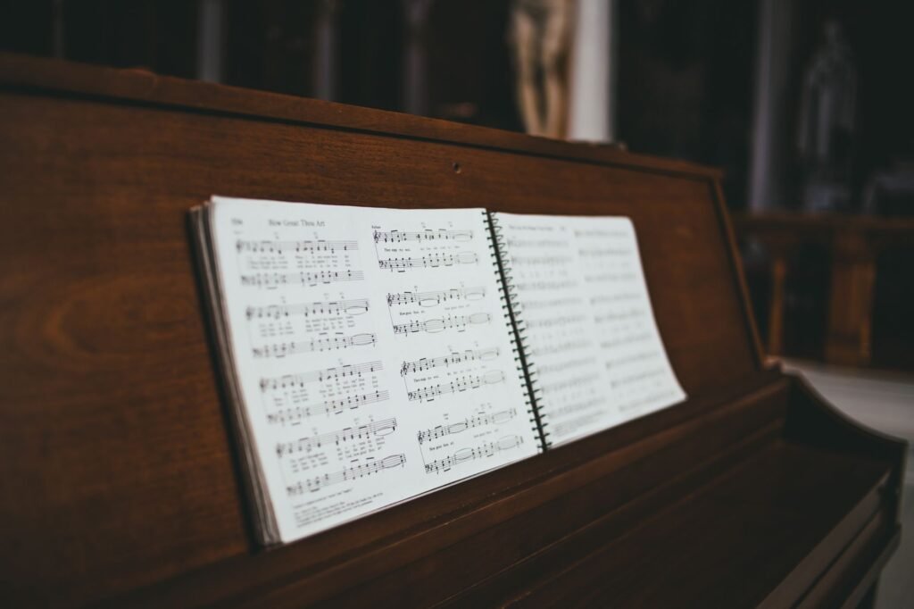 Open spiral book of sheet music propped on the stand of a wooden upright piano