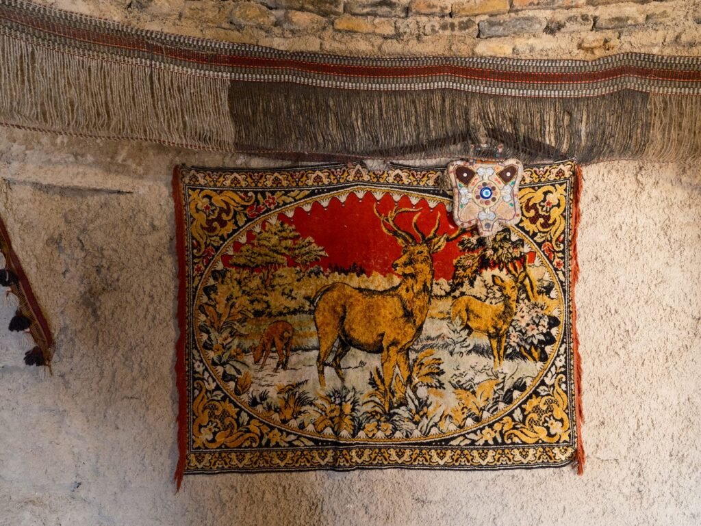 Colorful woven hanging with a deer scene and fringed edges mounted on a pale plaster wall