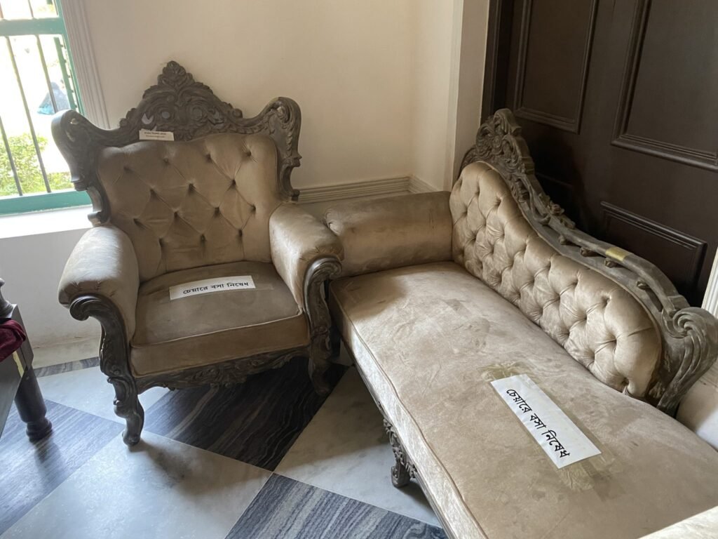 Ornate beige armchair and sofa with tufted upholstery, placed in the corner of a room with tiled floor. Lab...