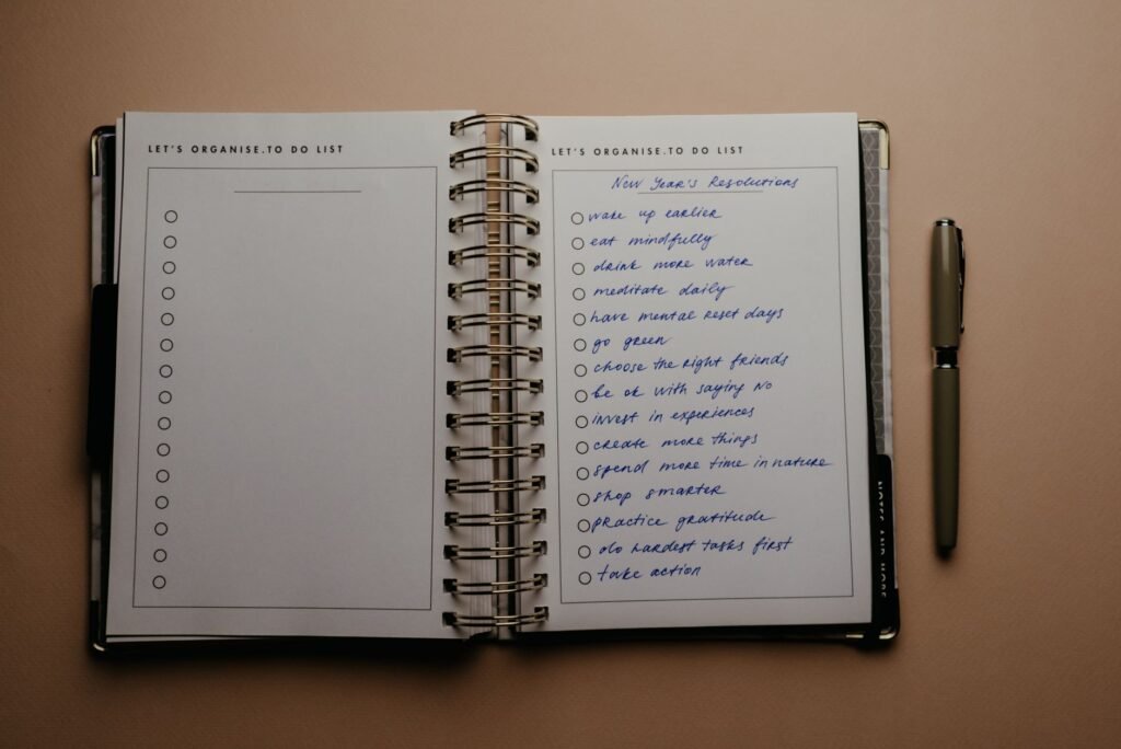 Open spiral planner with a handwritten list and a pen on a tan desk
