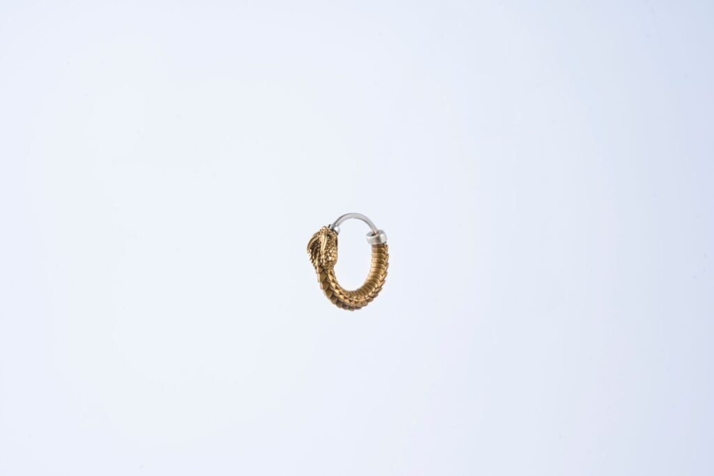 Single small twisted gold hoop earring floating against a plain pale background