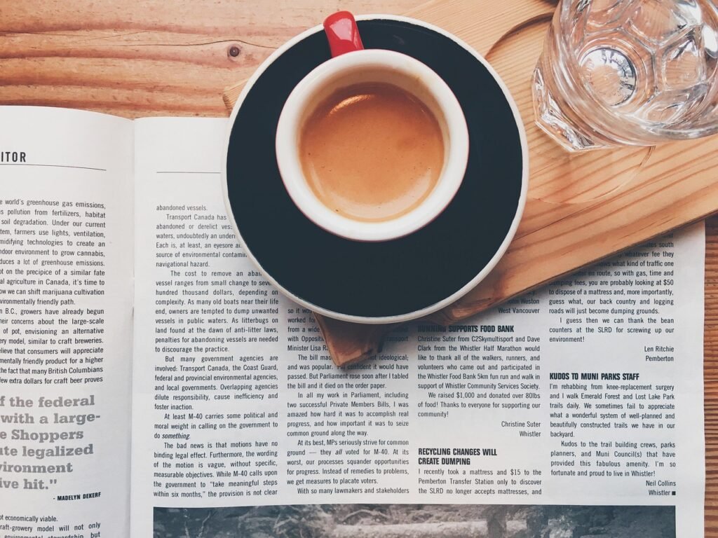 Open newspaper pages under a cup of coffee on a wooden table