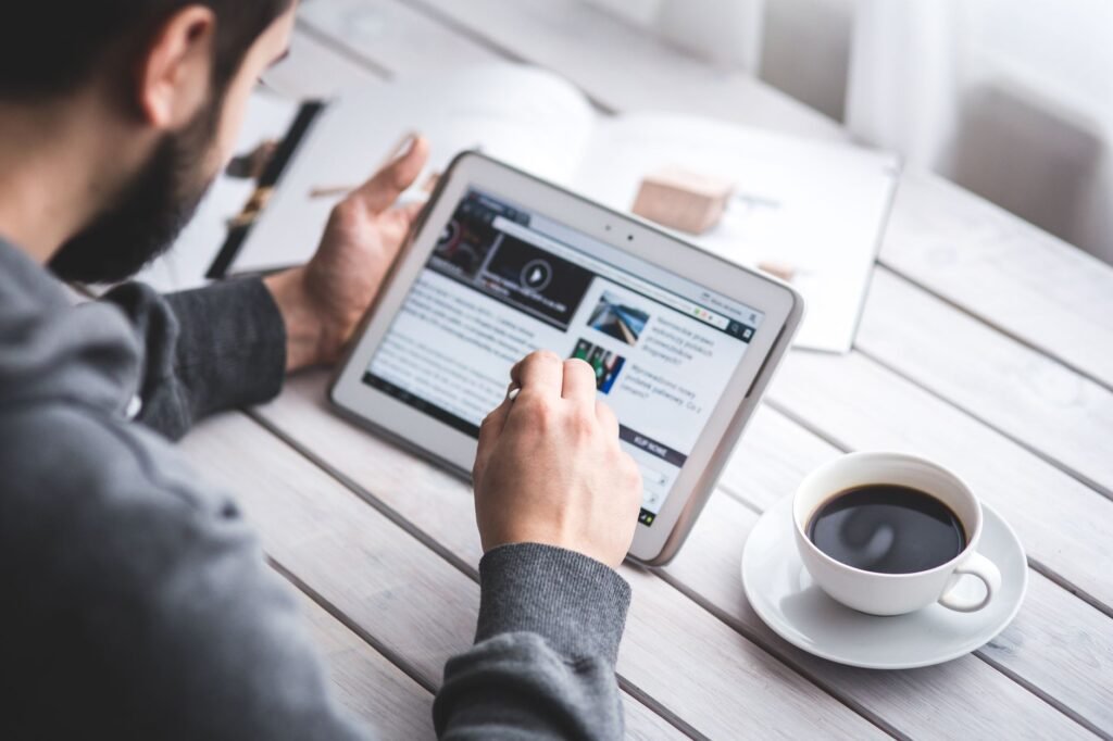 Man reading a news website on a tablet beside a cup of black coffee