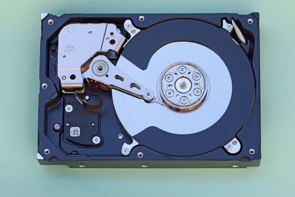 Opened hard drive showing the silver platter and read arm on a pale green background
