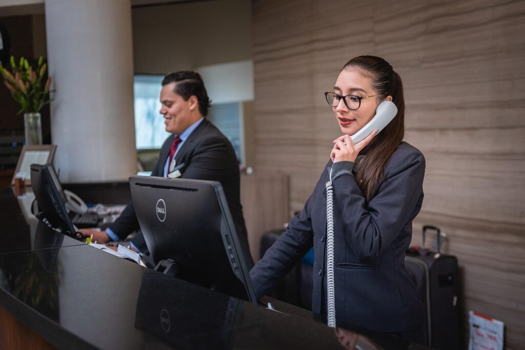 Two receptionists in dark suits working at a hotel front desk, one on the phone