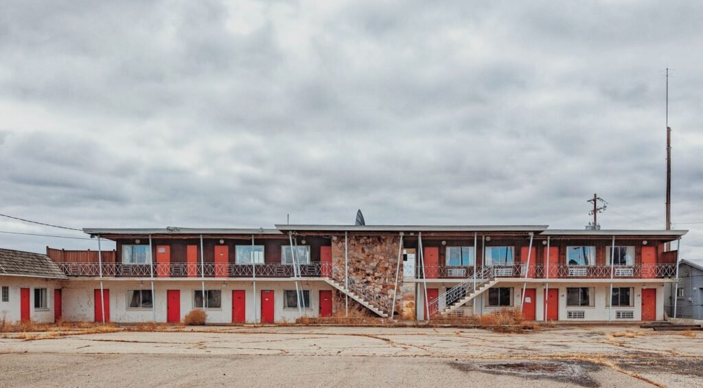 Two story motel with red doors facing an empty parking lot under cloudy skies