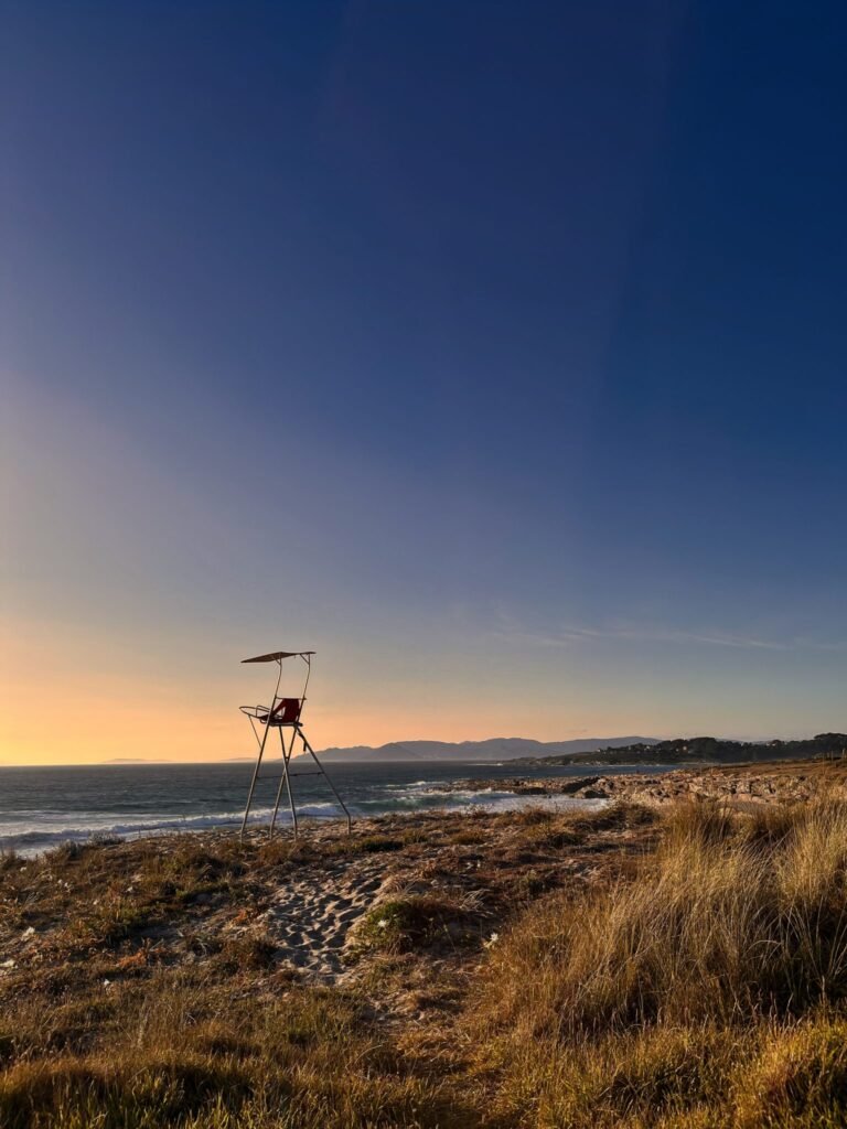 Empty lifeguard chair on a sandy, grassy Atlantic beach at sunset, with the ocean and mountains in the back...