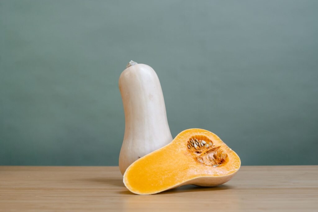 A whole butternut squash beside a halved one showing its seeds